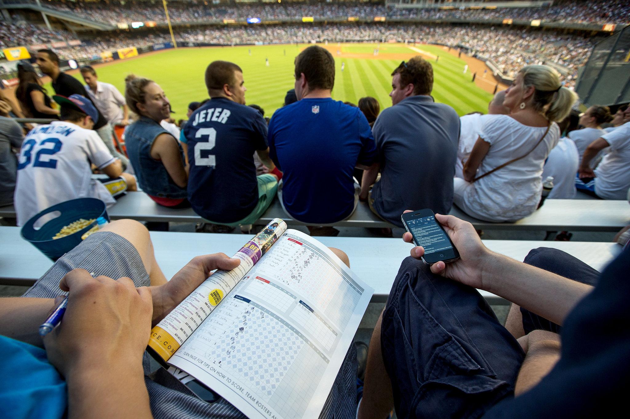 Fans keeping score and checking a phone during a baseball game